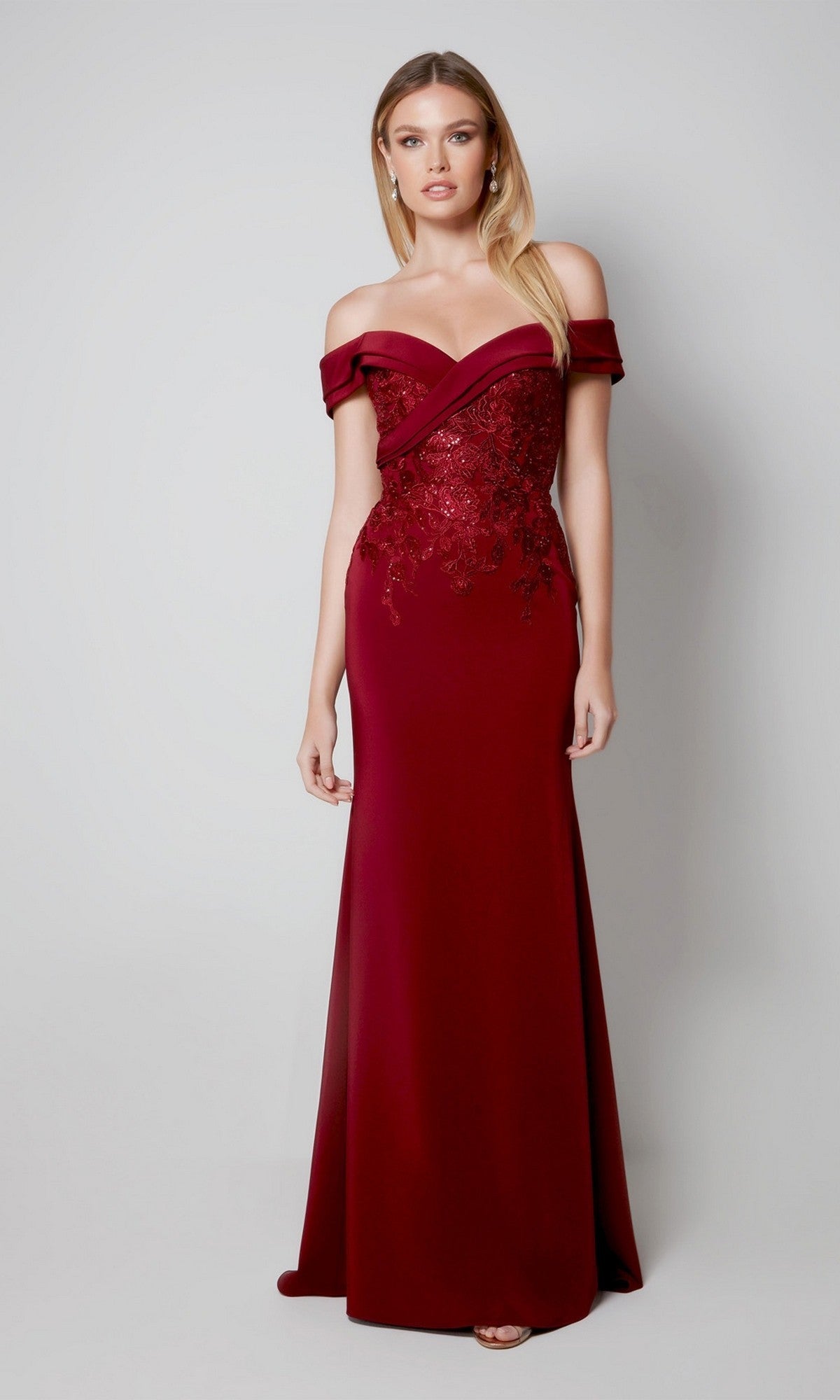 A woman stands against a plain light background, wearing the Alyce 27571 long formal dress—a floor-length burgundy gown in stretch-crepe with floral embroidery on the bodice.